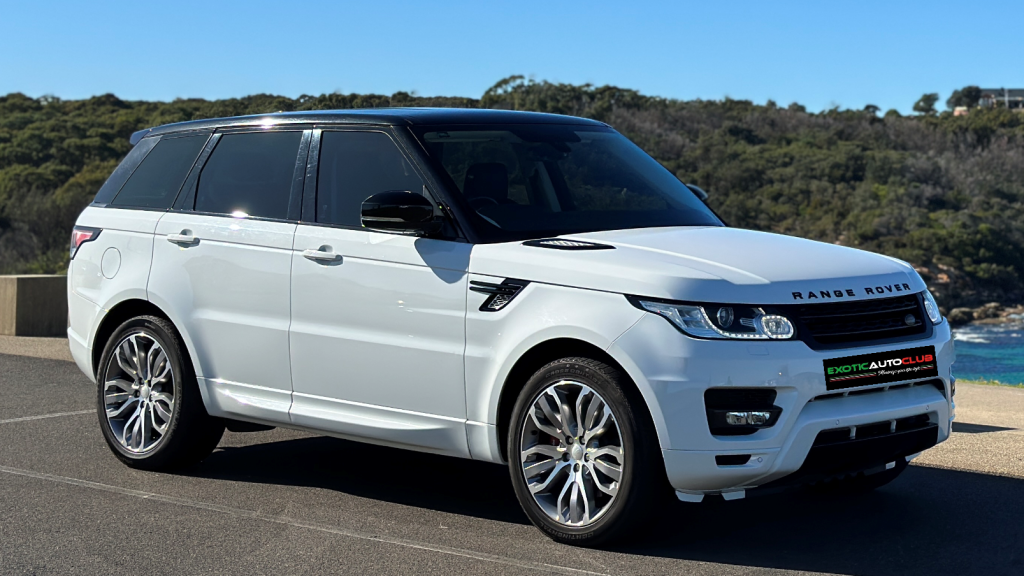 A white Range Rover SUV, boasting a black roof and tinted windows, is parked on a paved surface with greenery and a clear blue sky as the backdrop. The vehicle's sporty elegance is accentuated by the "EXOTIC AUTO CLUB" visible on the front license plate.