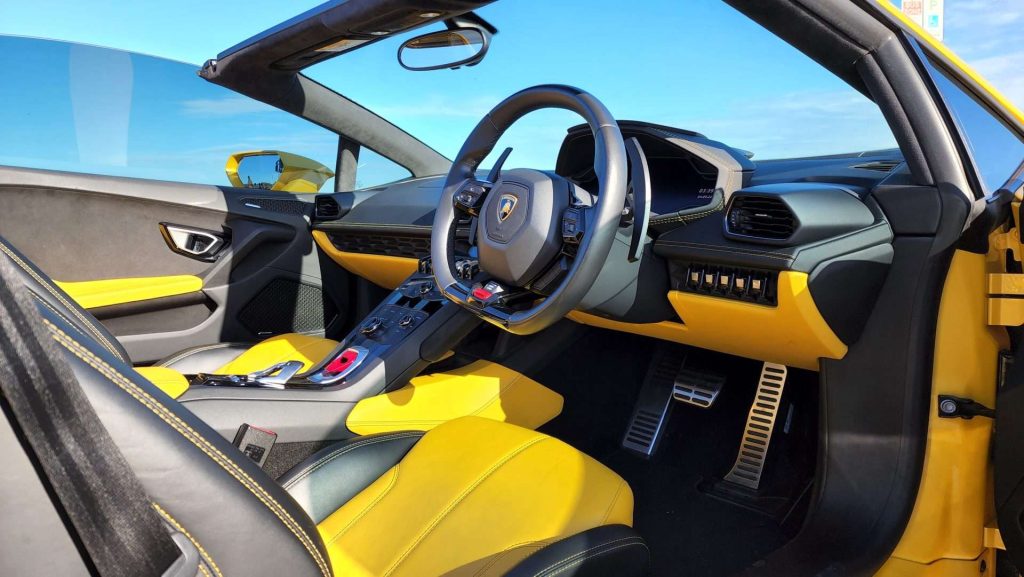 The interior of the Lamborghini Huracan Spyder boasts a luxurious yellow and black color scheme. With leather seats, steering wheel, dashboard, and control panel prominently displayed, the car's convertible top adds to its allure. The driver's door is slightly open, revealing the sleek design within.