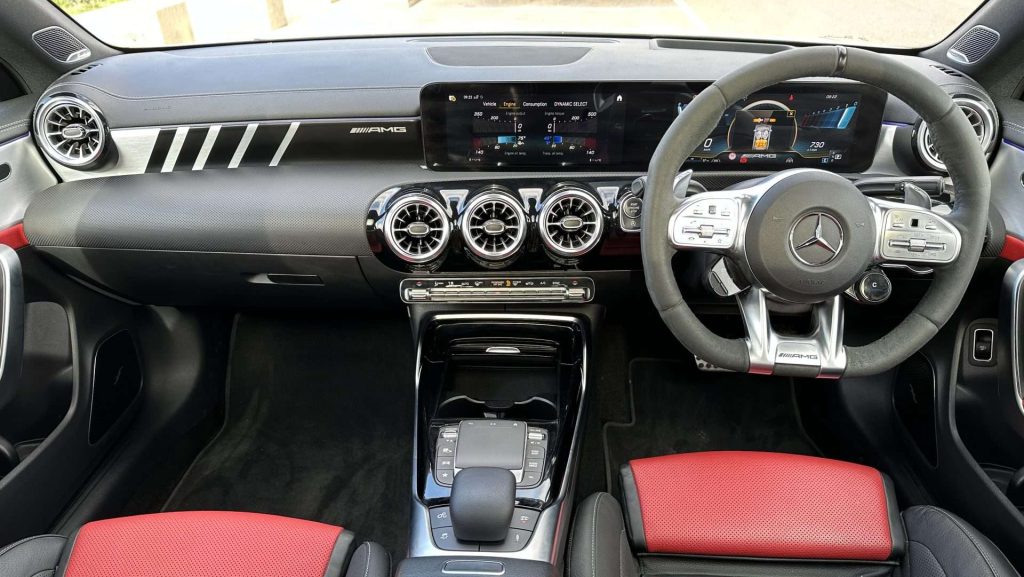 A modern car interior featuring a Mercedes-Benz AMG dashboard. The dashboard includes a digital display, air vents, and various controls. The steering wheel has multiple buttons, and the seats are upholstered in black and red. The center console of this Cla45s has additional buttons and controls.