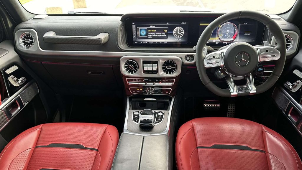 The interior of the Mercedes-Benz G63 AMG 55th Anniversary edition showcases a sleek black dashboard with touch screen displays, a multi-function steering wheel, and luxurious red leather seats. Controls for air conditioning, navigation, and other systems are conveniently located on the center console.